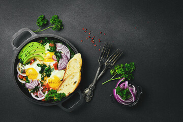 Nutritious Shakshuka breakfast with spinach and avocado in a metal pan. Traditional Jewish scrambled eggs. Top view, flat lay.