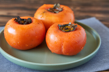 Ripe persimmons on a plate on a wooden background.