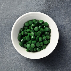 Close up of green spirulina pills in a bowl. On a dark concrete background.