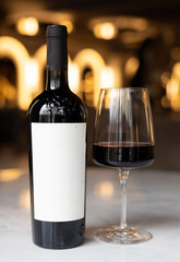 product photo of bottle with white label and glass with red white on hold in restaurant or in rack made from mirror. restaurant background, space for text, many bottles on shelf.