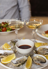 open oysters on plate with slice of lemon on ice cubes on table.candles in the chandelier in restaurant, woman hand taking dressing with spoon putting in sea fruit.romantic dinner