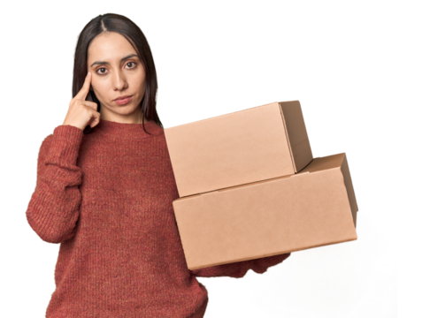 Caucasian young woman with moving boxes on studio background pointing temple with finger, thinking, focused on a task.