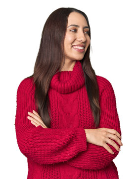 Young Caucasian woman in cozy red sweater on studio background smiling confident with crossed arms.
