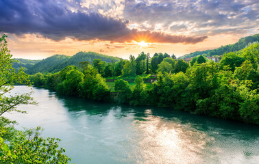 beautiful landscape of spring or summer sunset river with blue water and green hills on sides and...