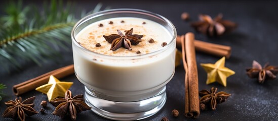 A glass of eggnog garnished with cinnamon sticks and star anise sits on a table. This festive drink is a popular holiday dessert made with eggs, milk, and spices