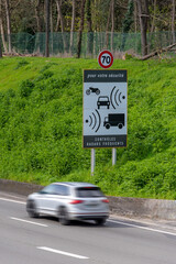 Voiture avec flou de mouvement passant devant un panneau de signalisation routière indiquant des contrôles de vitesse par radar au bord d'une route française - obrazy, fototapety, plakaty