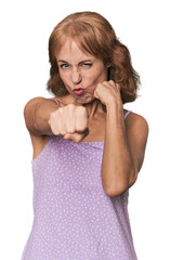 Redhead mid-aged Caucasian woman in studio throwing a punch, anger, fighting due to an argument,...