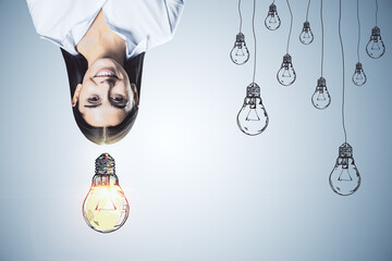 Upside down portrait of happy businesswoman with drawn light bulbs on concrete wall background....