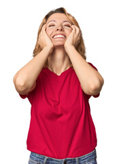 Blonde middle-aged Caucasian woman in studio laughs joyfully keeping hands on head. Happiness concept.