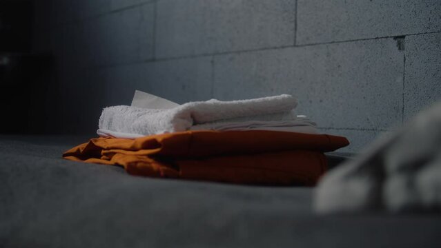 Close up of inmate placing orange prison uniform and bathroom accessories on bed. Guilty criminal or prisoner serves term for crime in jail. Detention center or correctional facility. Justice system.
