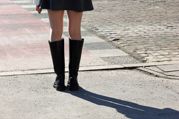 Female legs in black boots. Slim girl standing on a street, fashion in spring city