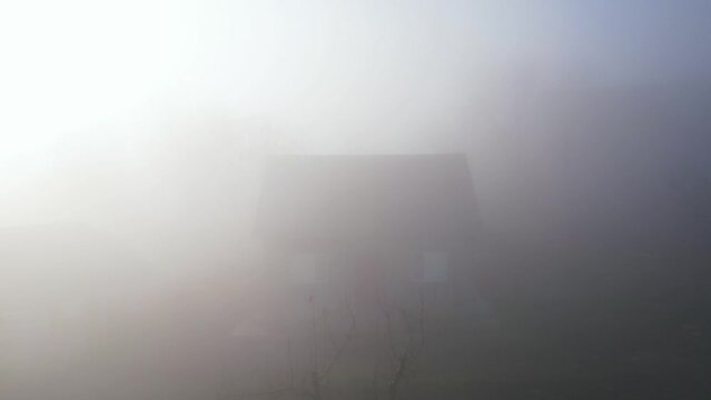 Mysterious house standing in fog with moonlight at dark night. Creepy atmosphere, house with windows in mist