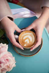 A cup of coffee in the hands of a girl on the cafe table. Aesthetically beautiful. The concept of a holiday, a date, a love story