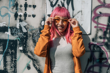 urban young woman with pink hair and vintage glasses at the wall