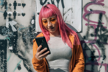 urban young woman with pink hair and phone on graffiti wall