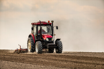 Focused farmer drives a modern tractor to till soil, preparing for sowing season - obrazy, fototapety, plakaty