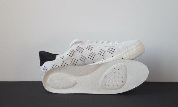 Leather orthopedic insole and white sport shoe on black white  background. Foot care accessories.