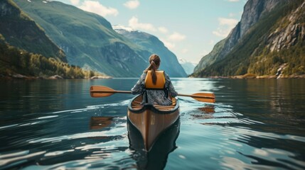 A person is actively paddling a canoe on a lake with majestic mountains in the background - obrazy, fototapety, plakaty