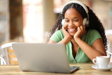 Happy black woman watching media using laptop and headphone