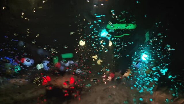 Winter night urban traffic scene as seen through the vehicle window covered with sleet drops. Melting snow water drips on the car windshield