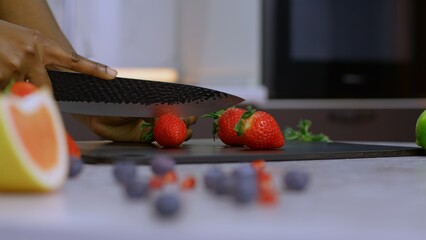 A knife cuts strawberries on a cutting board to decorate the dessert, we need to cut the strawberries into small slices with a knife, hands hold a sharp knife tightly and cut the strawberries.