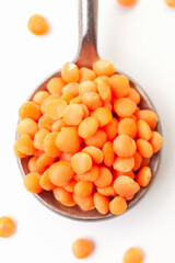 Dry red lentils in iron spoon on white background. Close-up