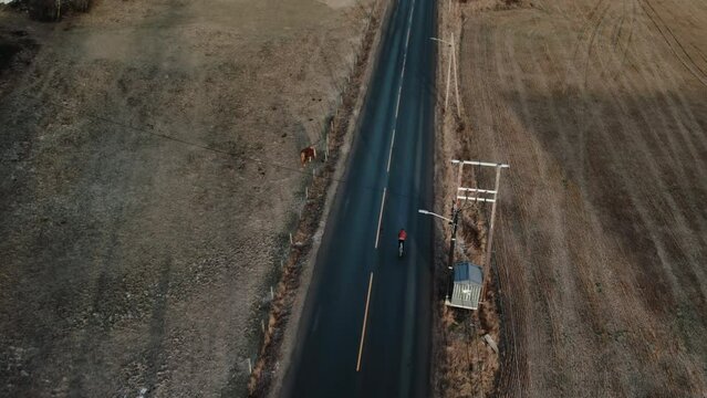 Aerial drone view on cyclist ride on empty country road, passing farm and horse ranch. Cinematic shot of cycling in autumn or early spring