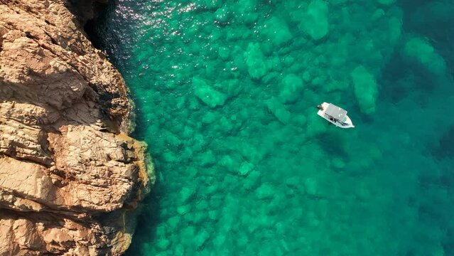 Boat floating on crystal clear waters near the rocky coasts of Girolata, Corsica, aerial view