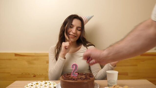 A girl sits in front of a table with a festive cake, into which a candle in the form of the number 24 is stuck. The concept of a birthday celebration.