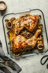 Roasted chicken legs with mushrooms in casserole  on rustic background, top view