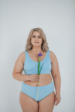 Plus size woman in lingerie holding flower against white background
