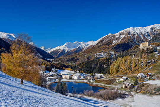 Tarasp Castle and lake near houses and snowcapped Silvretta Alps on sunny day, Tarasp, Lower Engadine, Engadine, Grisons, Switzerland