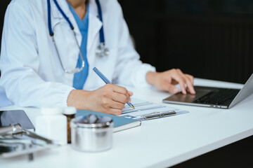 Doctor working on laptop computer and tablet and medical stethoscope on clipboard on desk, electronics medical record system EMRs concept.