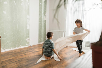 Boy pulling brother sitting on wallpaper and having fun at home