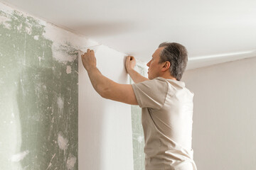 Man gluing white wallpaper in living room at home