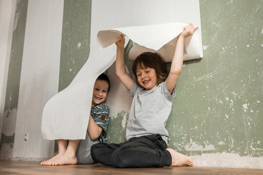 Cheerful brothers hiding under white wallpaper at home