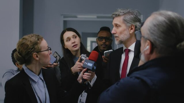 Busy American presidential candidate answers press questions and gives interview for media walking in parliament hallway. Confident politician surrounded by journalists. Election coverage. Slow motion