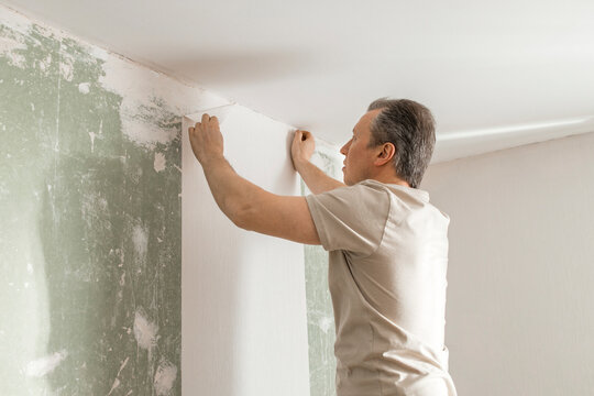 Man gluing white wallpaper in living room at home