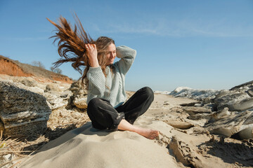 Woman sitting cross-legged on hill at windy sunny day