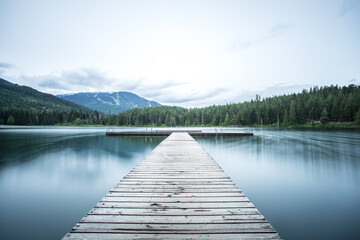 A long wooden pier on a smooth lake.  - Powered by Adobe