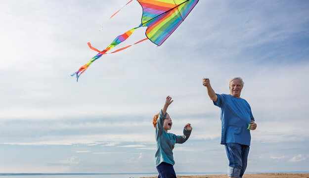 Elderly man flying kite with grandson at beach