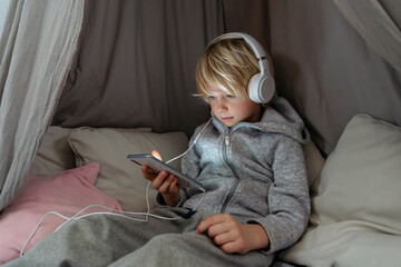 Boy wearing headphones using smart phone in canopy at home