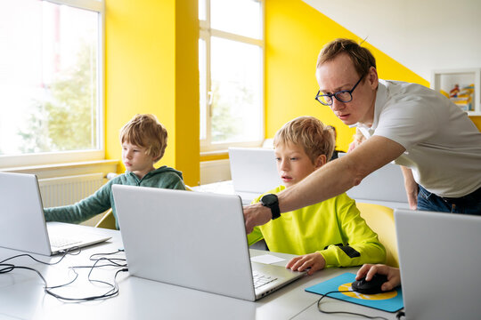 Professor teaching computer coding to boy with laptop in classroom