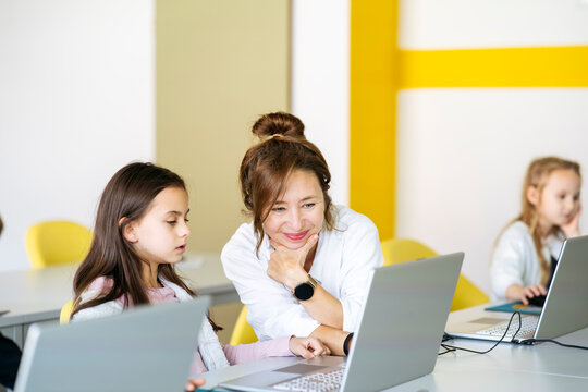 Smiling teacher teaching computer coding on laptop to girl in classroom