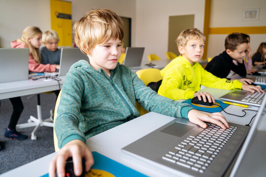 Blond boy using laptop learning computer programming at desk in classroom