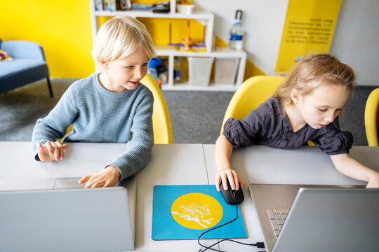 Boy and girl sitting at desk with laptops learning computers in classroom