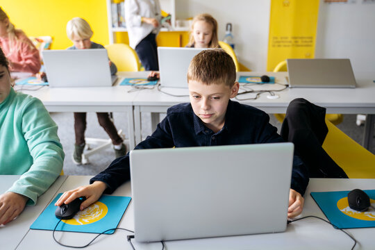 Dedicated boy using laptop learning computer programming at desk in classroom