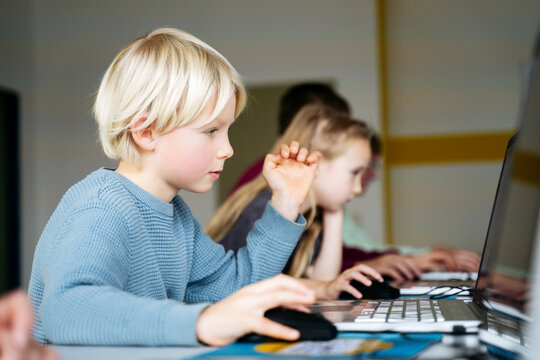 Blond boy learning coding through laptop desk in classroom
