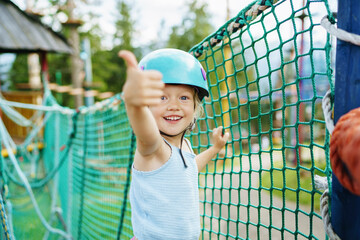 Excited smiling girl showing thumbs up gesture near net at rope park