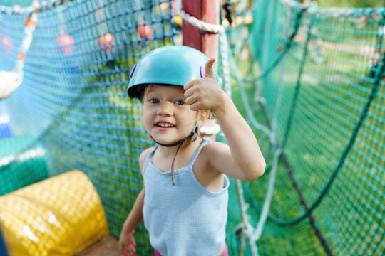 Cute girl wearing helmet and showing thumbs up gesture at rope park